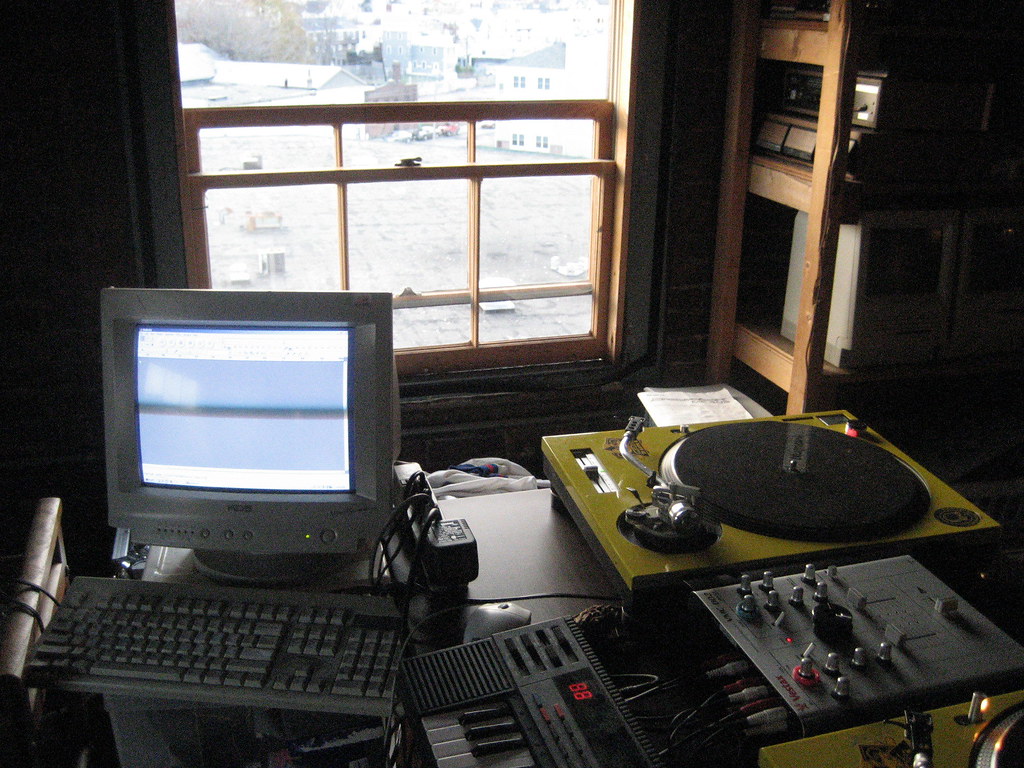 Un ordinateur, du matériel son et musique, sur une vieille table devant une fenêtre.